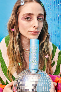 A girl leaning on a blue bottle of hair oil with a disco ball.
